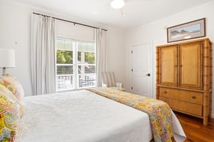 Main floor queen bedroom with hardwood floors and a large window bringing in natural light.