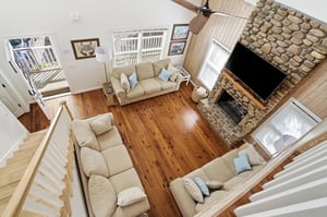 View from the upper landing looking down into the living room, highlighting the tall ceilings and stone fireplace.