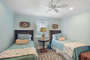 Guest bedroom with two twin beds, ceiling fan, shutters, and hall bathroom access.