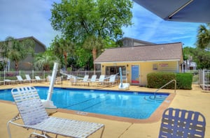 Seasonally heated pool with lounge chairs, palms, and clubhouse access nearby.