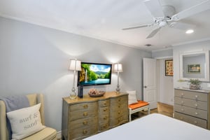 Primary bedroom angle with dresser storage, TV, window seating, and closet access.