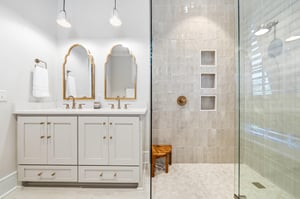 Two sinks sit beneath shaped mirrors with goldtoned fixtures.