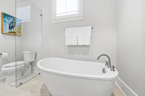 A tall shuttered window brings daylight beside the separate glass shower.