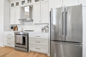 A Frenchdoor refrigerator and range sit beneath tall white cabinetry.