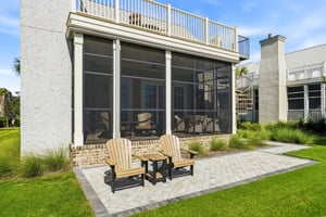 Two chairs sit just outside the screened porch beside the lawn.