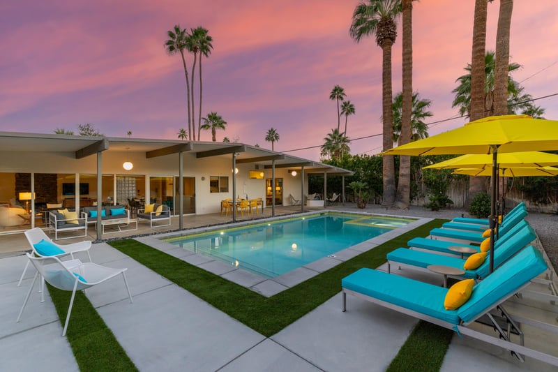 Modern desert oasis with sparkling pool and vibrant loungers beneath swaying palms at sunset.
