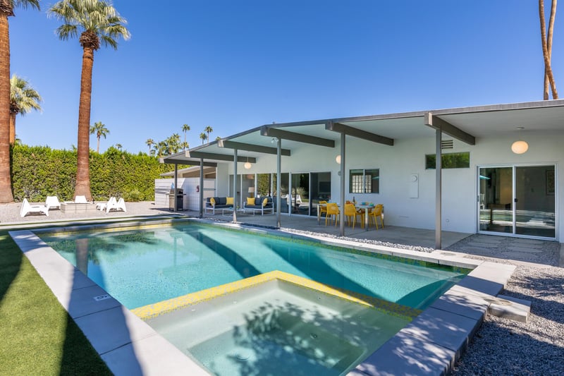 Modern desert oasis with sparkling pool and spa surrounded by swaying palm trees under endless blue skies.