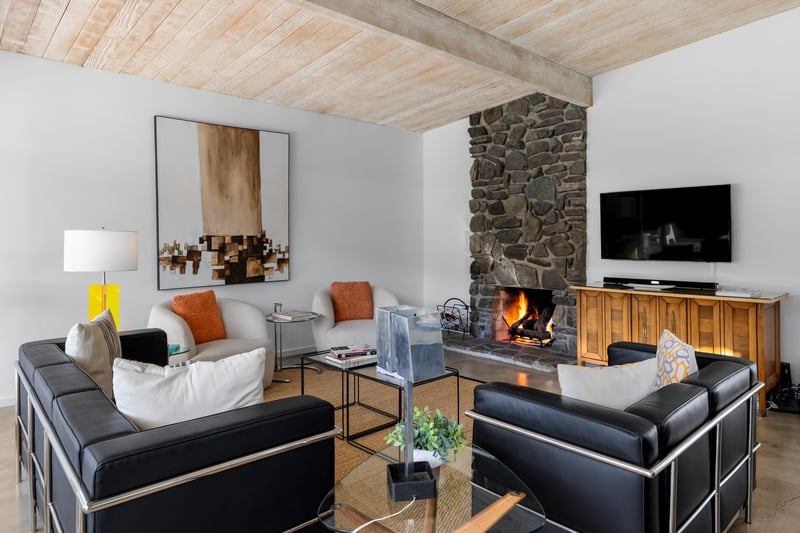 Cozy up by the crackling stone fireplace in your stylish living room, where modern comfort meets rustic charm beneath beautiful wood beam ceilings.