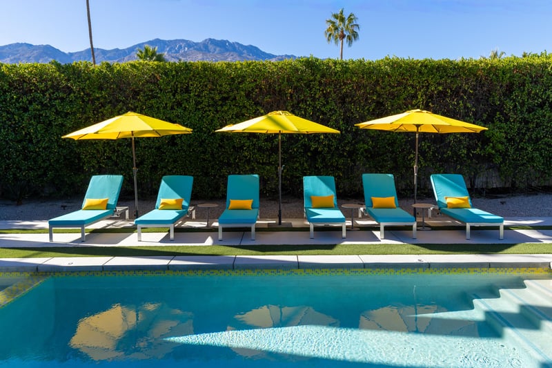 Pristine poolside setting with turquoise loungers and sunny yellow umbrellas, framed by desert mountains for the perfect Palm Springs retreat.