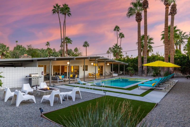 Modern desert retreat showcasing a stunning swimming pool area surrounded by towering palm trees against a vibrant sunset sky.