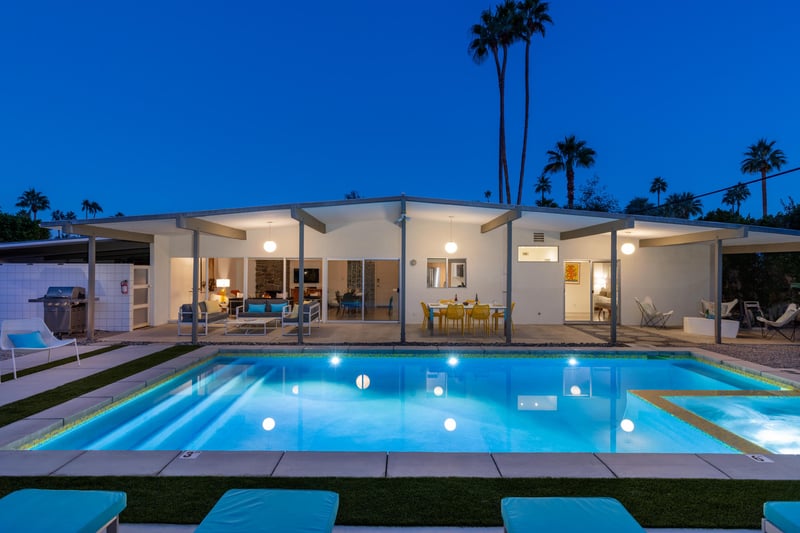 Modern desert retreat featuring a stunning illuminated pool beneath towering palms and starlit skies.