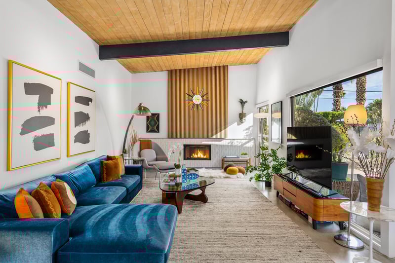 Unwind in this stunning living room featuring a cozy fireplace, plush blue sectional, and warm wood ceiling beams that create the perfect retreat.