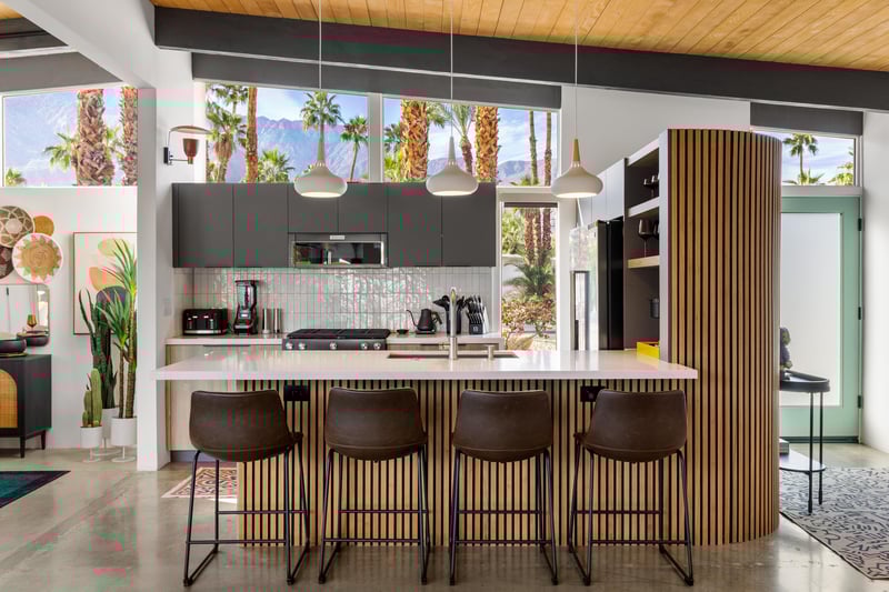 Your sleek modern kitchen features premium appliances and a stunning breakfast bar, all framed by desert palms through floortoceiling windows.