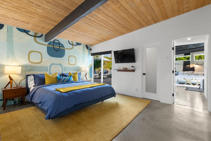 Drift off in this stylish bedroom featuring vibrant blue bedding, modern artwork, and warm wood ceilings that create your perfect retreat.