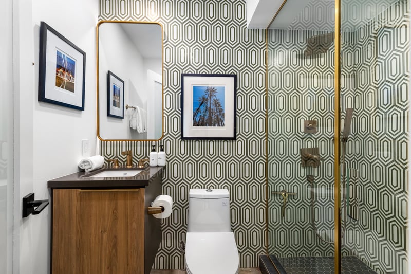 Step into your stylishly designed bathroom featuring geometric wallpaper, elegant brass fixtures, and thoughtful artwork creating a sophisticated powder room experience.