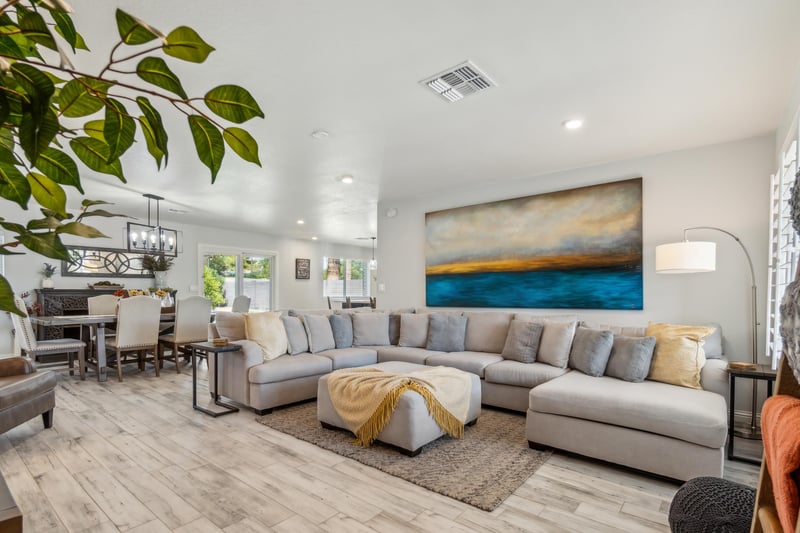 A modern, openconcept living and dining area. A large gray sectional sofa with pillows and a cushioned ottoman.