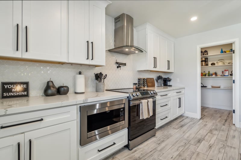 Modern kitchen with white cabinetry and sleek black handles. The kitchen has a stainless steel range and matching microwave.