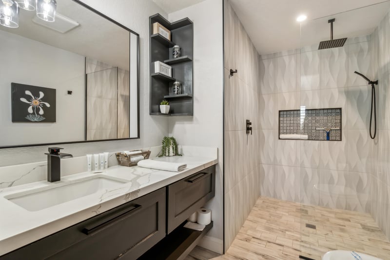Master bathroom features a sleek vanity with a white marble countertop and dark cabinetry, offering a clean and modern look. A large mirror above the vanity adds to the sense of space and brightness in the room.