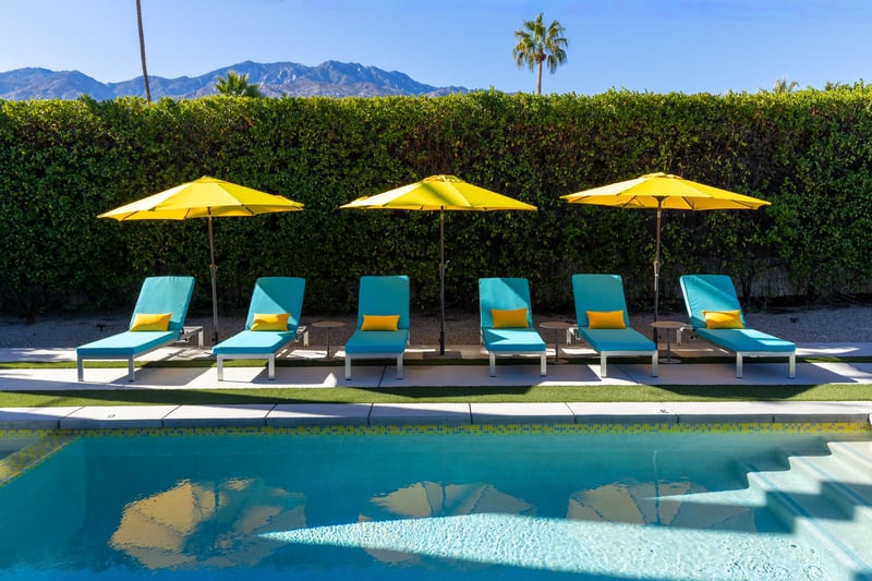 Pristine poolside setting with turquoise loungers and sunny yellow umbrellas, framed by desert mountains for the perfect Palm Springs retreat.