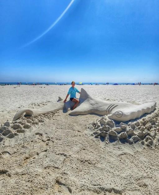 person sitting on a large sand shark sculpture on the beach in Gulf Shores, Alabama