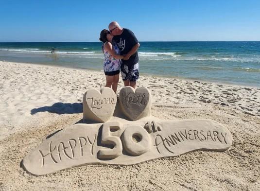 couple kissing next to a custom 50th anniversary sand sculpture on the beach in Gulf Shores, Alabama