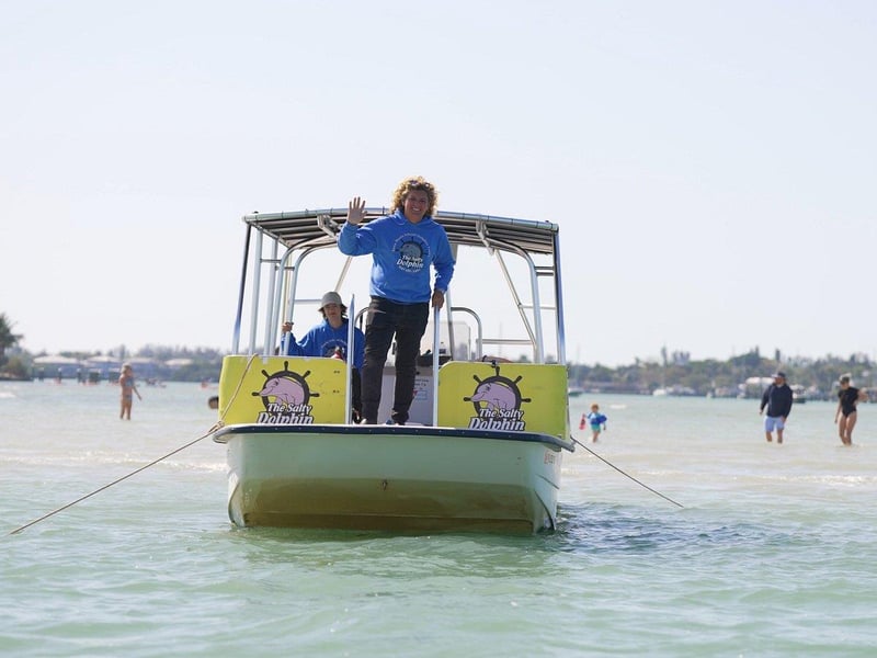 Sandbar tour boat anchored in shallow water with guests wading and relaxing around the boat.