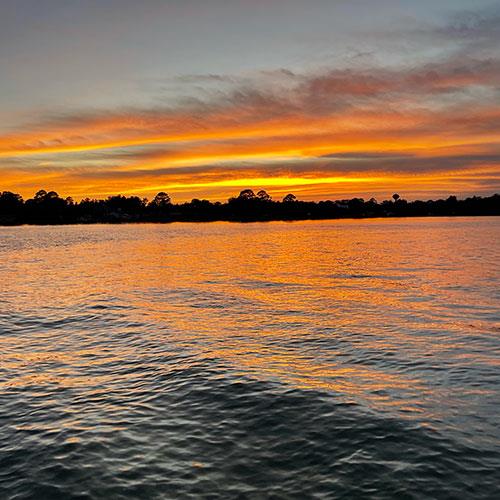 Vibrant orange and gold sunset reflecting across smooth coastal waters at the end of a sunset cruise.