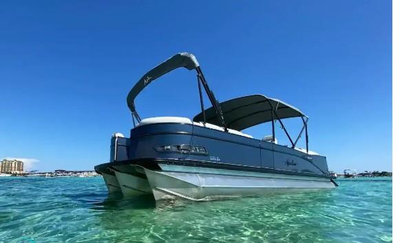 Luxury Avalon tritoon pontoon boat anchored in shallow emerald water under a clear blue sky.