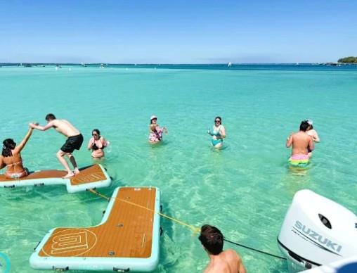 Friends playing and standing on floating dock mats in shallow water at Crab Island near a pontoon boat