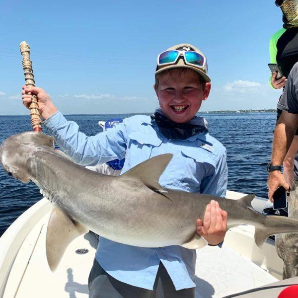 Smiling boy on a fishing boat holding a shark he caught offshore in the Gulf of Mexico.