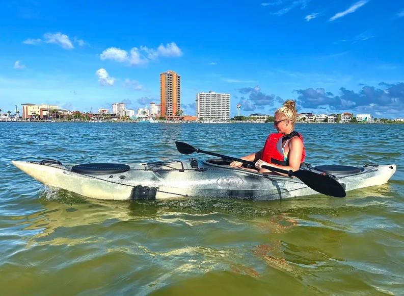 Woman kayaking in calm bay waters with Pensacola Beach skyline in the background.