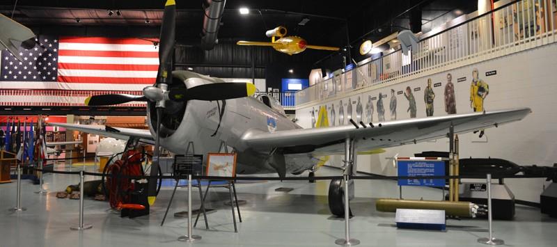 Military aircraft exhibit inside museum with American flag backdrop and informational displays