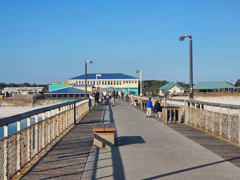 People walking and fishing along Okaloosa Island Pier with beach buildings in the distance