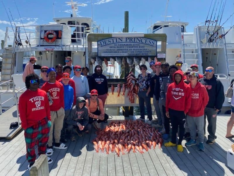 A group standing in front of the Destin Princess sign with fish on the wooden dock in Destin, Florida