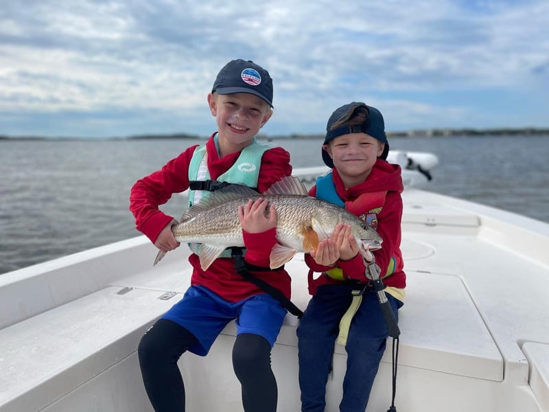 Two kids showing off their catch on board a CB fishing charter