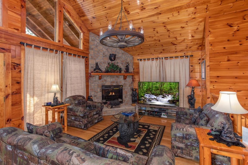 Living room with corner stone fireplace and wagon wheel chandelier at Bear Country, a 3bedroom cabin rental located in Pigeon Forge