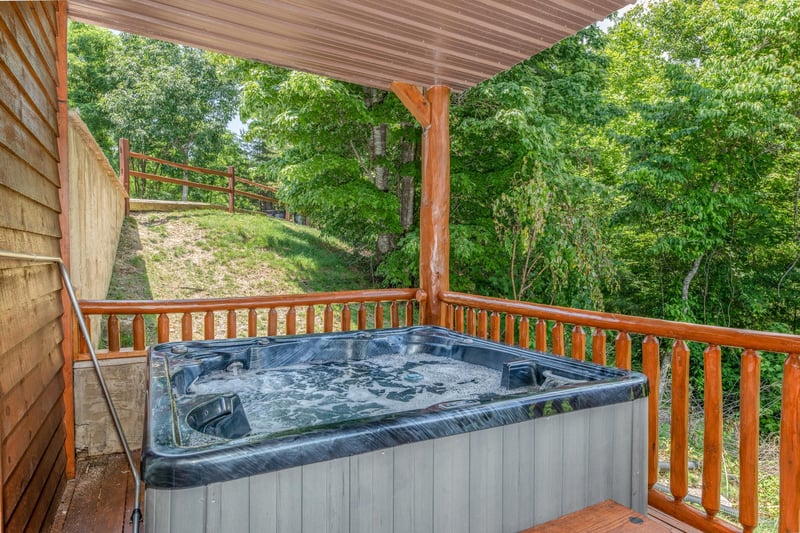 Hot tub on a covered deck with the yard behind it at Gods Country, a 4 bedroom cabin rental located in Pigeon Forge