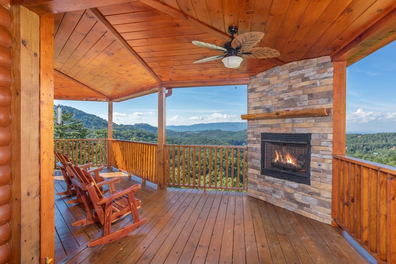 Outdoor fireplace and rocking chairs on the covered deck at Four Seasons Palace, a 5bedroom cabin rental located in Pigeon Forge