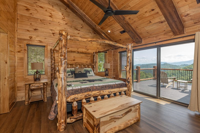 Four post log bed, night stands, lamps, chest, and deck access in a bedroom at Black Bears  Biscuits Lodge, a 6 bedroom cabin rental located in Pigeon Forge